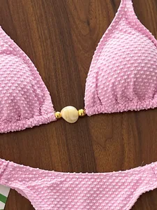 Close-up macro detail of a pink textured bikini top featuring a shell bead ornament