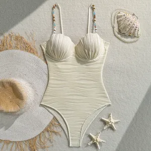 Vista detallada de un elegante bañador crema con copas de concha y tirantes de cuentas