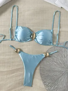 Detailansicht eines hellblauen glänzenden Bikinis mit dekorativen goldenen Metallschnallen