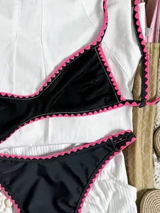 Detailansicht eines schwarzen Bikinis mit rosa bestickter Borte auf weißem Hintergrund