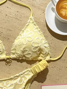 Primer plano de bikini amarillo con bordado floral y amuleto de oro