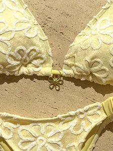 Primer plano detallado de un bikini amarillo con bordado floral y colgante dorado