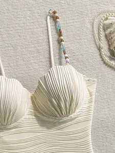 Detalle en primer plano del bañador crema con copas de concha y tirantes de cuentas finas