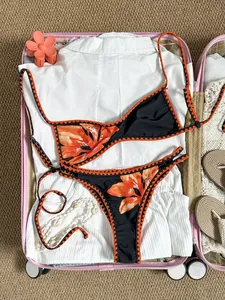 Detailansicht eines Retro-Floral-Bikinis mit orangefarbenen Stickereien in einem rosa Koffer
