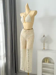 Detailed view of white leaf-patterned lace trousers and crochet bikini top on a mannequin stand