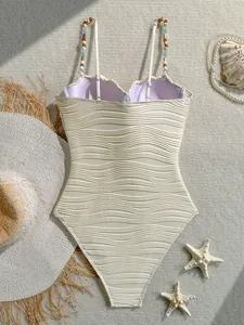 Detalle de bañador blanco con textura de ondas, tirantes con cuentas y copas de concha.