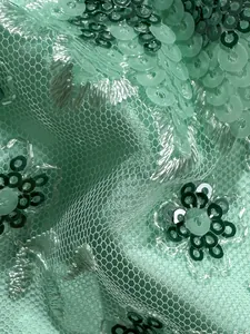 Detalle macro de bordado de flores con lentejuelas verde menta sobre tejido de malla.