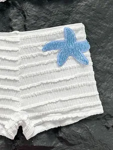 Détail d'un short de bikini blanc côtelé avec un patch étoile de mer bleu à paillettes