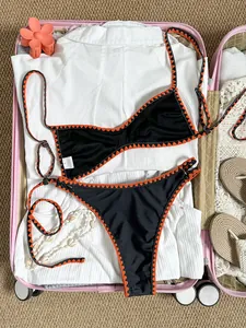Detailansicht eines schwarzen Bikinis mit orangen Häkelkanten im rosa Koffer.