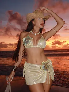 Close-up detail of champagne gold shiny bikini set with blue floral embroidery at sunset beach