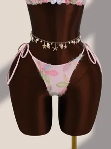 Gros plan du bas de bikini rose brodé de fleurs avec une chaîne de taille coquillage