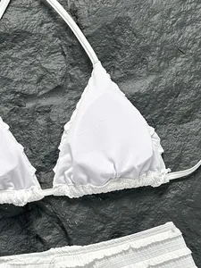 Détail de bikini blanc à volants sur fond de roche sombre texturée, idéal pour la plage.