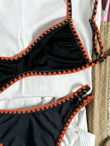 Detailansicht eines schwarzen Bikinis mit orangefarbenem Stickereirand auf Weiß.