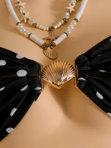 Gedetailleerd beeld van zwart polkadot bikinitopje met een elegante gouden schelpgesp