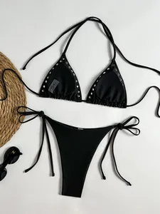 Flat lay of black halter bikini set with silver metal studs and beach accessories