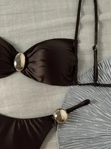 Detailaufnahme eines glänzenden braunen Bikini-Oberteils mit goldener Metallschnalle.