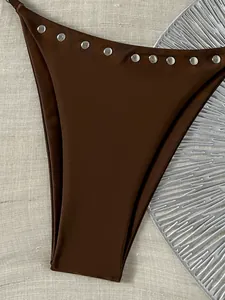 Close-up detail van een donkerbruin bikinibroekje met decoratieve zilveren klinknagels