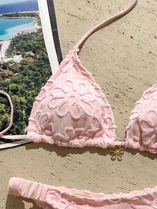 Primer plano de un bikini rosa con bordado floral 3D y dije decorativo de flor oro.
