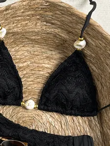 Detailweergave van een zwarte kant bikini met gemarmerde kralen en gouden accenten