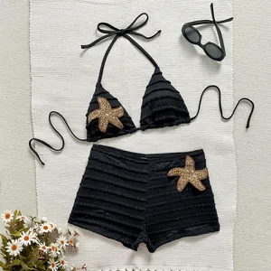 Détail d'un bikini noir côtelé deux pièces avec des écussons étoiles de mer dorés.