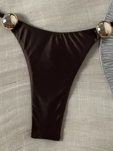 Makro-Detail des glänzenden dunkelbraunen Bikini-Unterteils mit goldener Verzierung