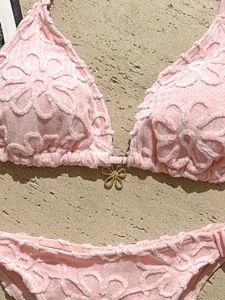 Detalle de un conjunto de bikini rosa con textura floral y un colgante de flor dorada.