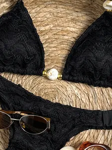 Detailopname van een zwarte kanten bikinitop met elegante marmeren kralen en goudaccenten