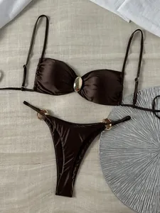 Nahaufnahme eines glänzenden schokoladenbraunen Bikinis mit eleganten goldenen Metallakzenten