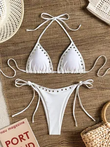 Detail of a white two-piece bikini set with silver rivet studs on a woven straw mat