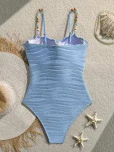 Vista detallada de un bañador azul claro con textura ondulada y tirantes de cuentas finas.