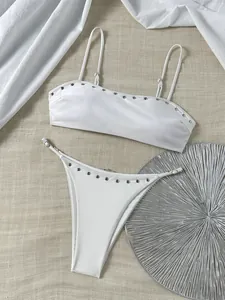 Detailopname van witte bikini met klinknagels op getextureerde beige stoffen achtergrond.