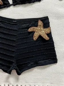 Gros plan sur un bas de bikini noir côtelé avec un écusson étoile de mer en paillettes