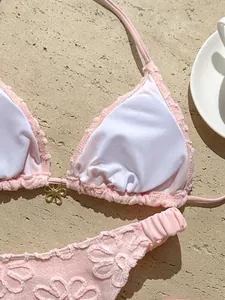 Primer plano de un bikini rosa con bordados florales y colgante de flor dorada