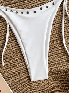 Close-up of white bikini bottom with silver metal studs on straw background