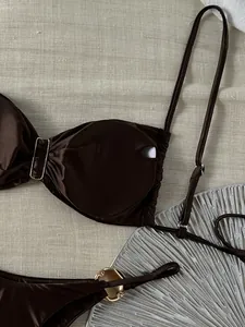 Detailaufnahme eines glänzenden dunkelbraunen Bikini-Oberteils mit goldener Metallschnalle