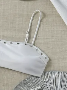 Detailopname van een witte bikini-top met zilveren klinknagels en verstelbaar bandje.