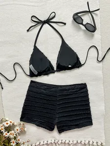 Bikini deux pièces noir à volants avec haut licou et short sur tapis blanc