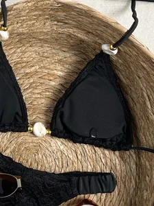 Detailopname van een zwarte bikinitop met textuur en marmeren kralen op stro-achtergrond