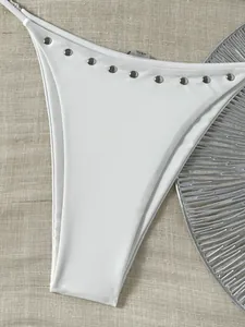 Gedetailleerd overzicht van wit broekje van bikini met zilveren klinknagels op stof