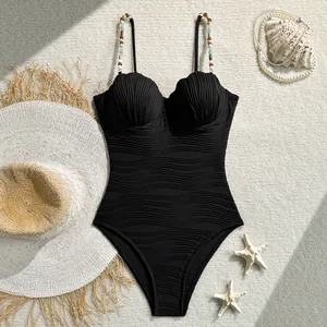 Detalle de bañador negro con textura de ondas, copas de concha y tirantes de cuentas.