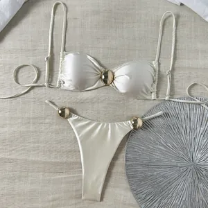 Detail des glänzenden weißen Satin-Bikini-Sets mit eleganten goldenen Metallschnallen