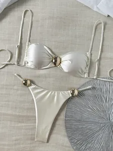 Detailansicht eines weißen Satin-Bikini-Sets mit goldener Hardware auf Leinen
