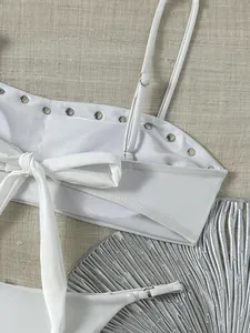 Close-up van witte bikinitop met zilveren klinknagels en strik op getextureerde basis.