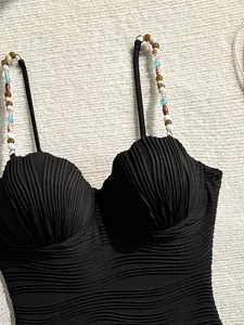 Primer plano de bañador negro con textura de ondas, copas de concha y cuentas