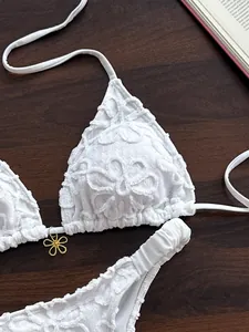Detalle de bikini de encaje bordado blanco con dije de flor dorada decorativa