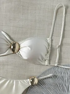 Detailansicht eines weißen glänzenden Bandeau-Bikinis mit einem goldfarbenen Metallornament