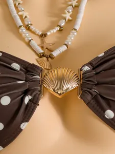 Detailweergave van bruine bikini-top met stippen en gouden schelpsluiting met kettingen