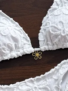 Primer plano muy detallado del bikini de encaje blanco con colgante de flor dorada