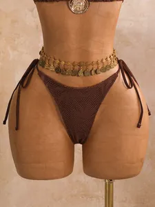 Detailopname van een bruin gehaakt bikinibroekje met gouden muntentailleketting
