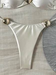 Detailansicht weißer Bikini-Slip mit glänzendem Finish und goldfarbenen Kugel-Dekoren.